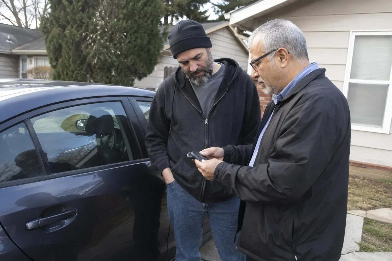 Two adults discussing a key fob beside a parked car. — Car Lockout Service, Brampton