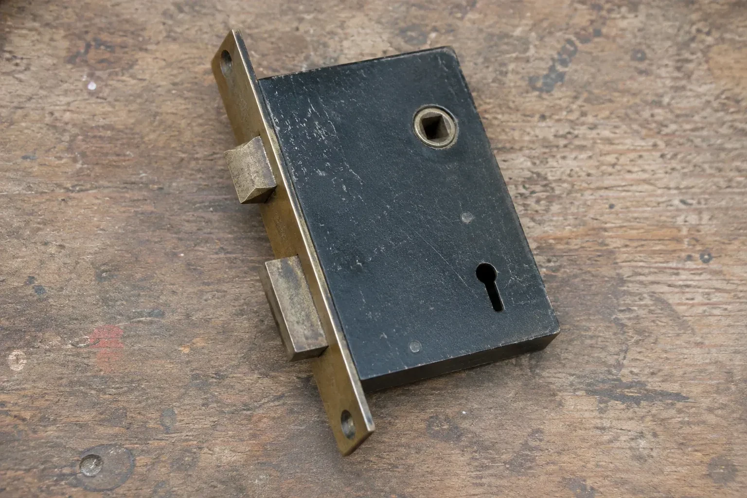Closed mortise lock case with spindle opening, keyhole, latch and deadbolt on a wooden workbench. — Vintage Mortise Lock Service, Brampton